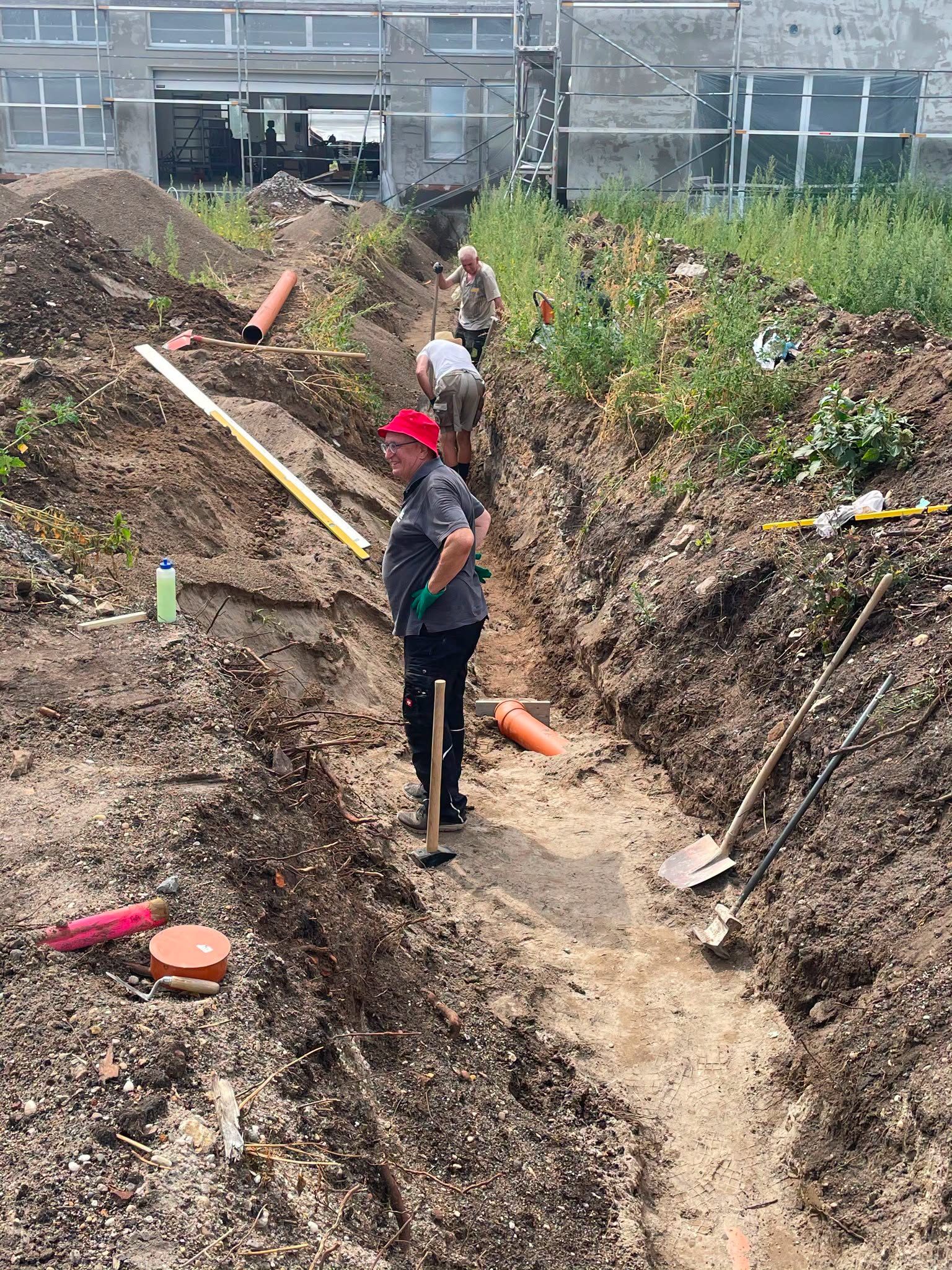 Helfer im Graben vor dem Neubau beim Verlegen der Abwasserleitung