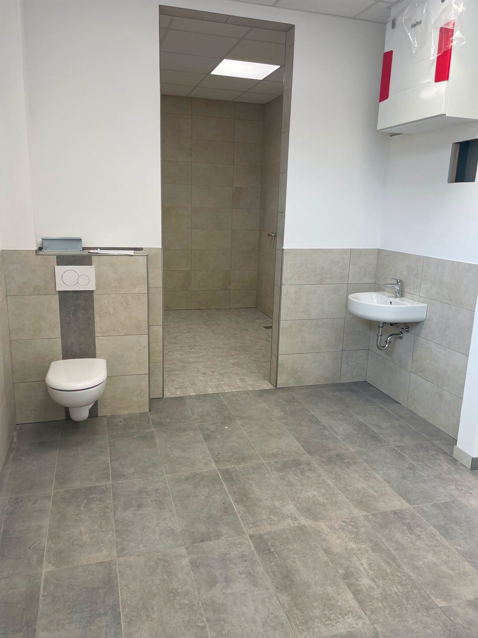 Gefliester Sanitärbereich mit WC, Waschbecken und Durchgang zur Dusche