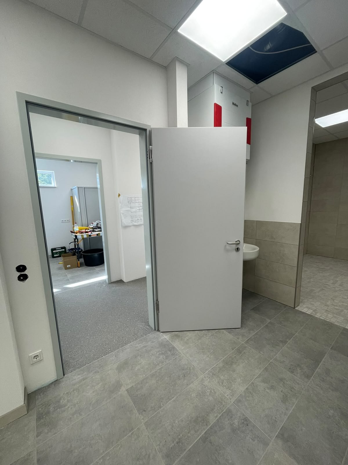 Geöffnete neue Tür im gefliesten Vorraum mit Blick in den Nachbarraum